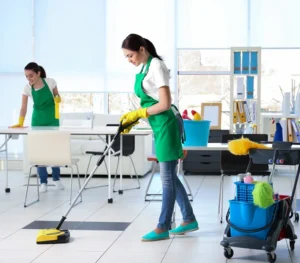 Reinigungskräfte in grünen Schürzen bei der gründlichen Oberflächenreinigung in einem modernen Büro.